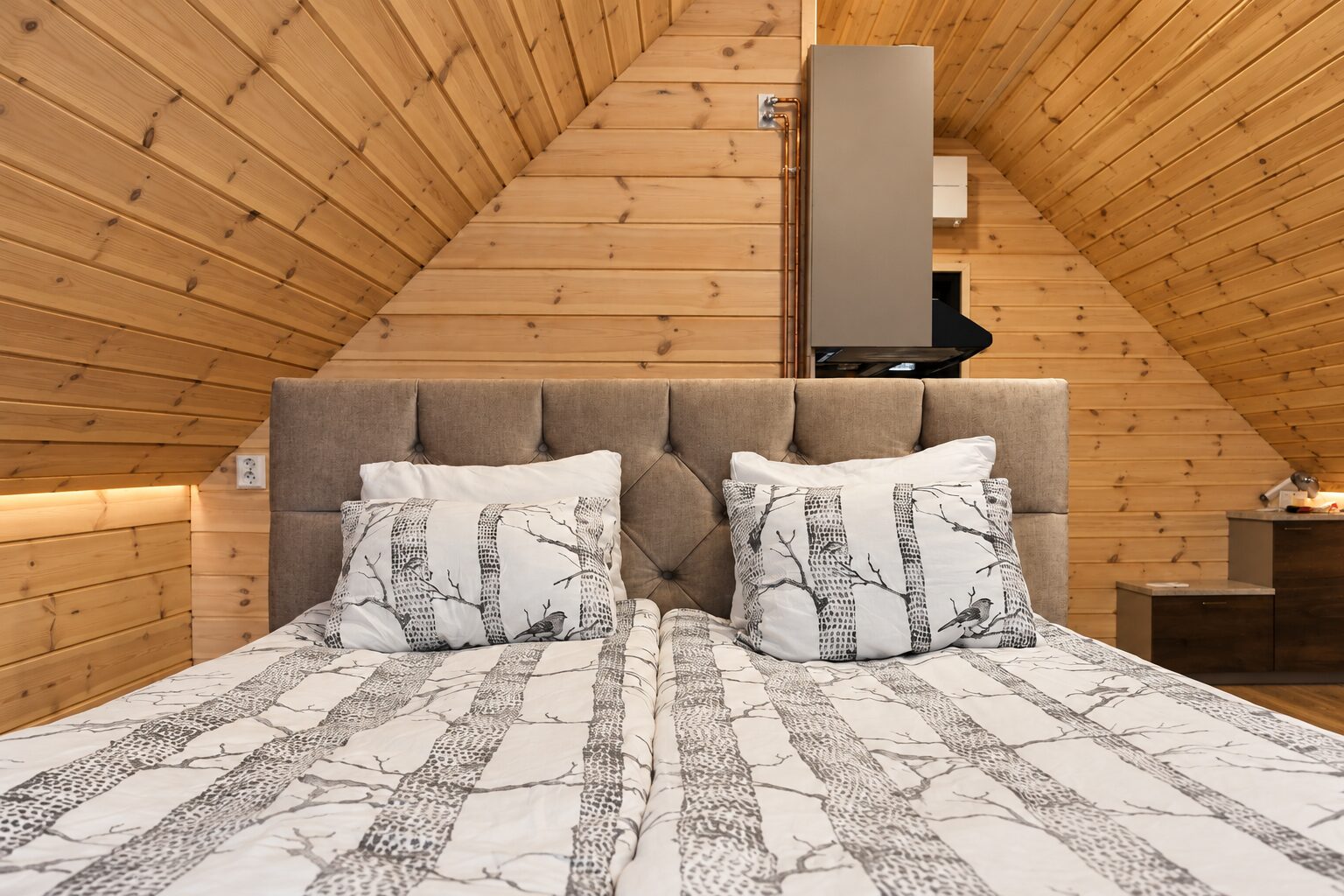 Parisänky verhoillulla päädyllä ja koivukuvioisilla vuodevaatteilla puupaneloidussa makuutilassa